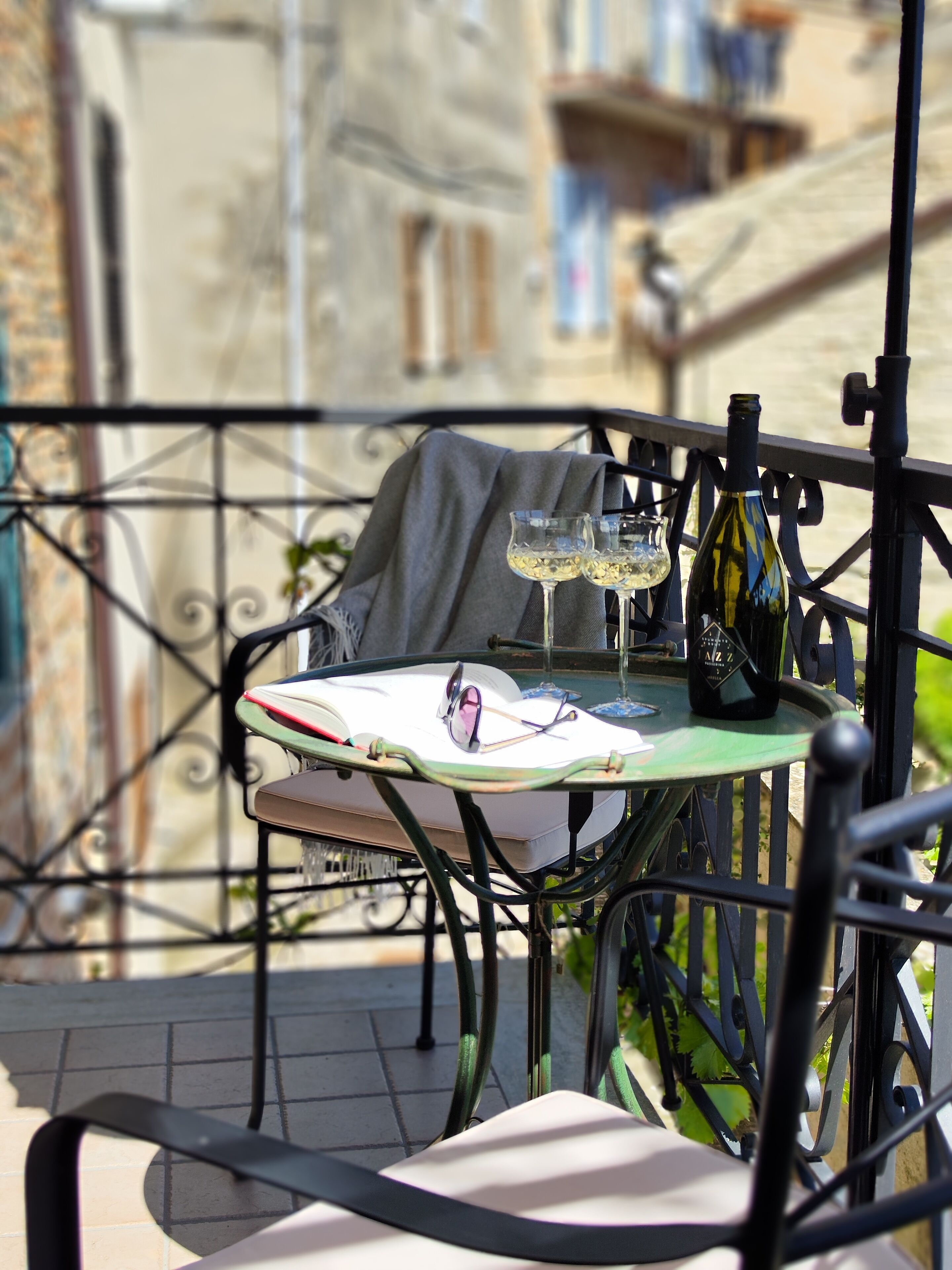 A table with a wine bottle and glasses on a balcony with a metal railing.