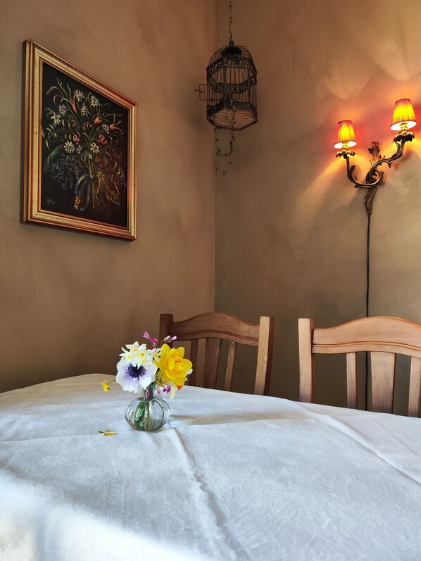 A dining area with a table set for two, a framed painting on the wall, a hanging light fixture, and a wall-mounted lamp. - Casa Agello B&B (Ripatransone)