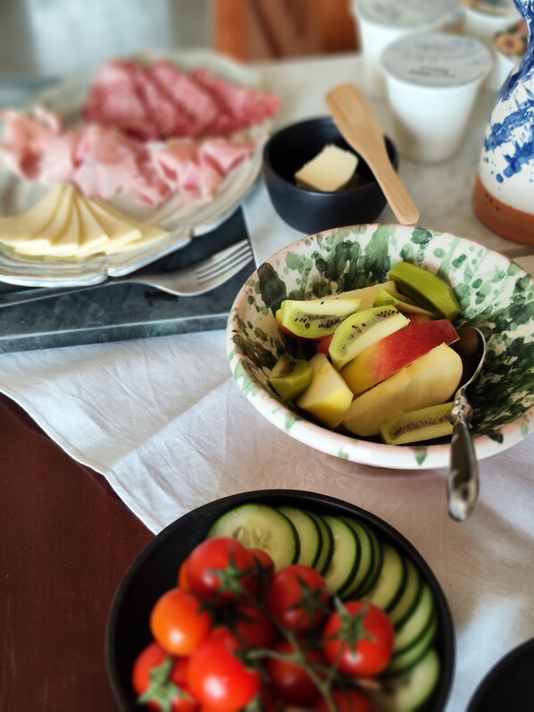 A table with various food items including a bowl of sliced fruits, a plate of cherry tomatoes, and a plate of sliced cucumbers.