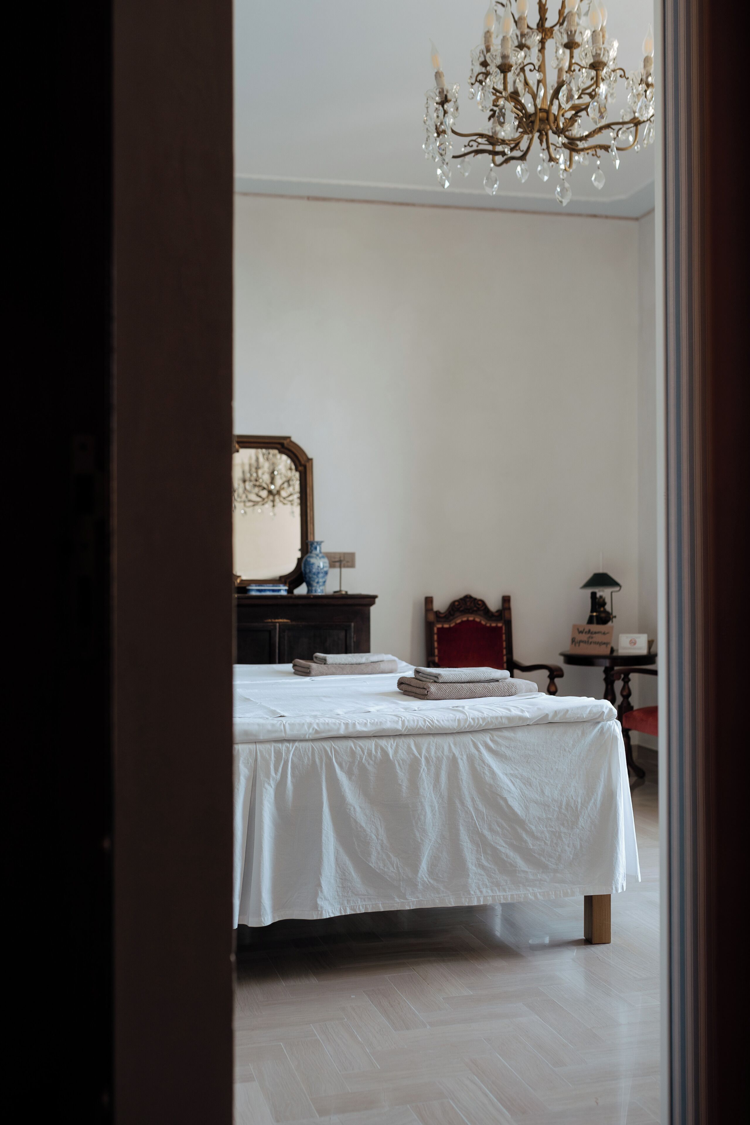 Un dormitorio con una cama, un tocador, un espejo, una silla roja y una araña.