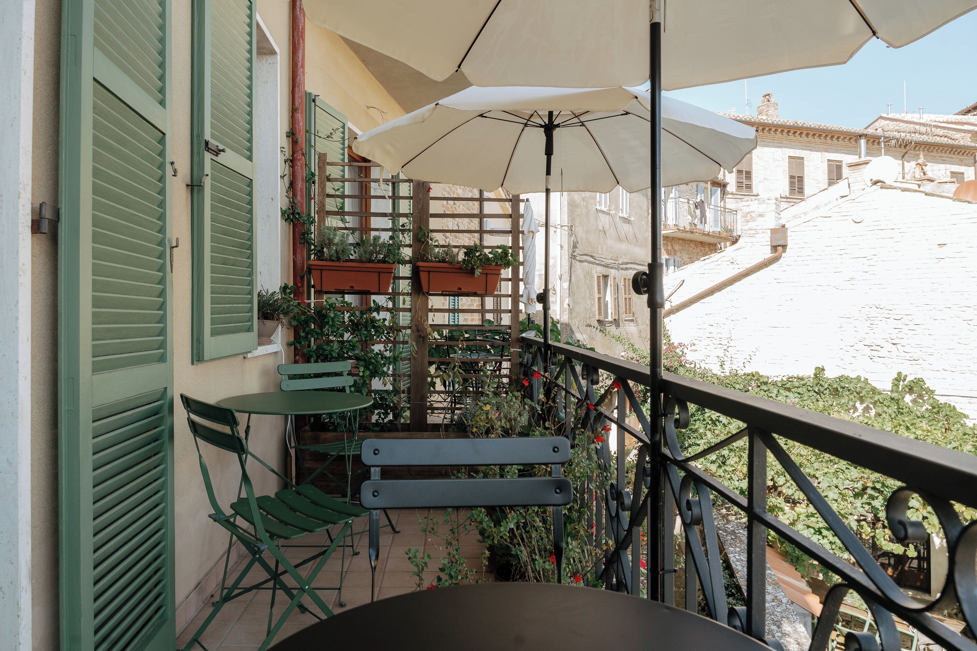 A balcony with a table, chairs, and an umbrella. There are potted plants and a view of a building in the background.