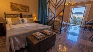 Camera d'albergo con un letto grande, una panca in legno, un lampadario, vista sull'esterno e un balcone con tavolo e sedie.
