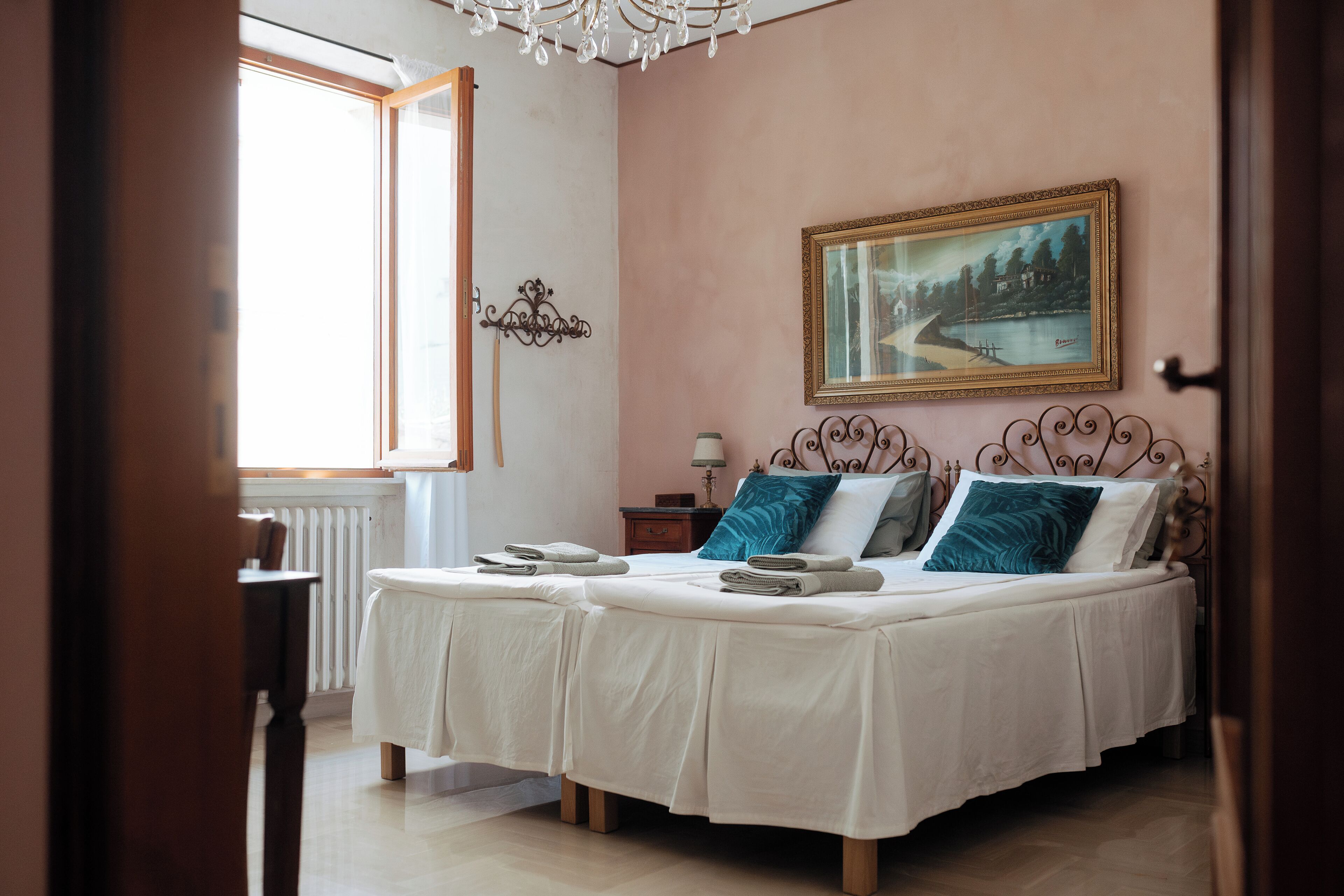 A bedroom with two beds, a painting on the wall, and a window with curtains.