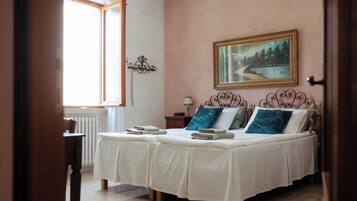 A bedroom with two beds, a painting on the wall, and a window with curtains.
