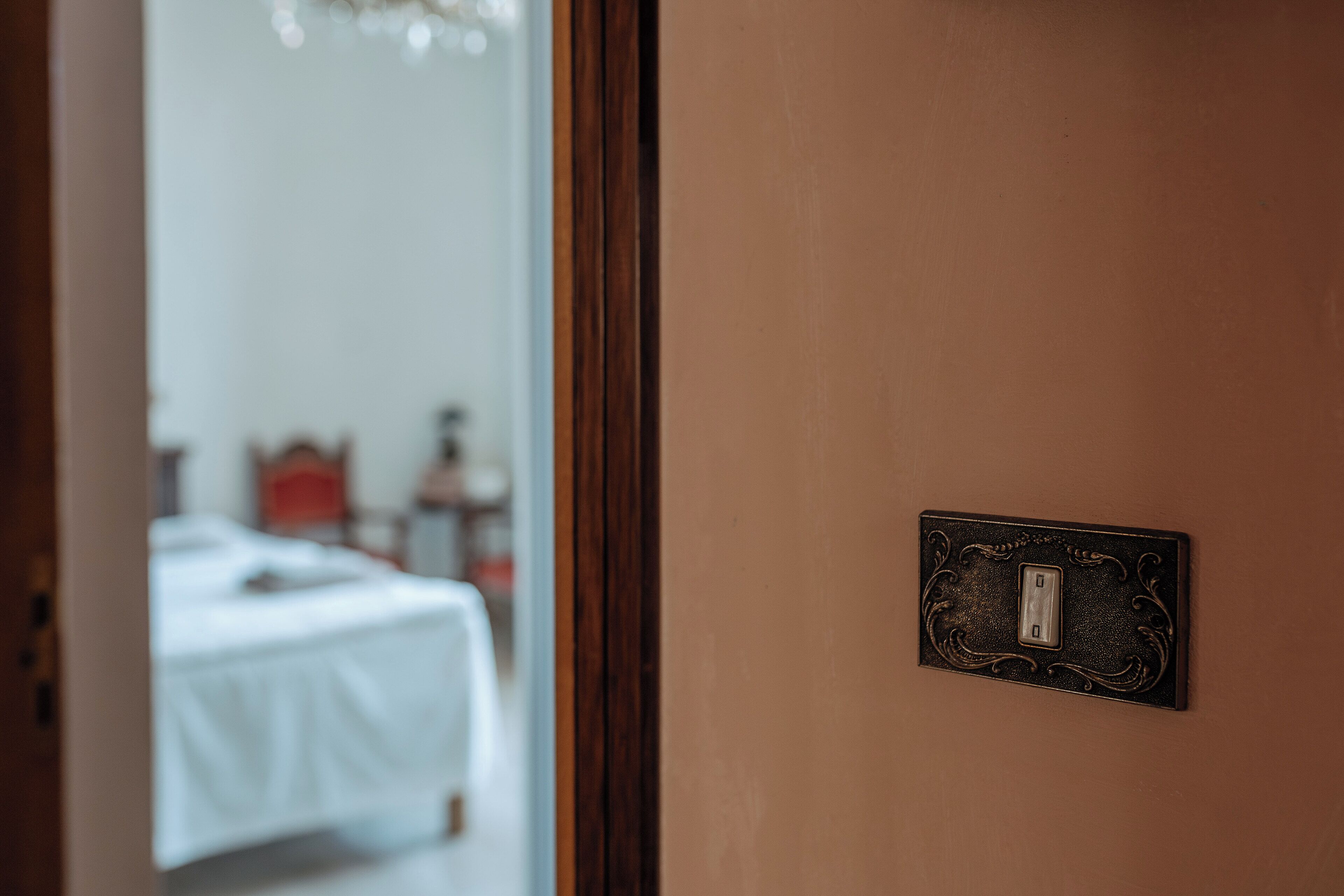 Uma porta com interruptor de luz e vista para um quarto com cama e cômoda.