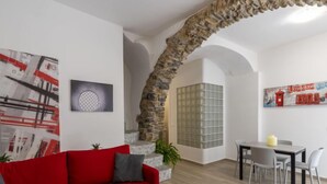 A living room with a red sofa, a stone archway, a dining area with a table and chairs, and a wall with a cityscape painting. - Il Giardino by Interhome (Terzorio)