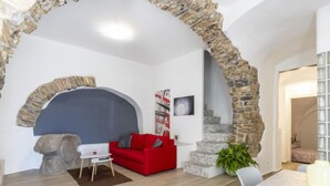 A modern living room with a stone archway, a red sofa, a coffee table, and a staircase leading to another room. - Il Giardino by Interhome (Terzorio)
