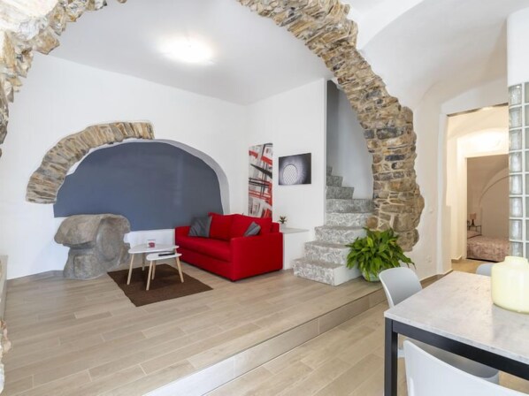 A modern living room with a stone archway, a red sofa, a coffee table, and a staircase leading to another room.