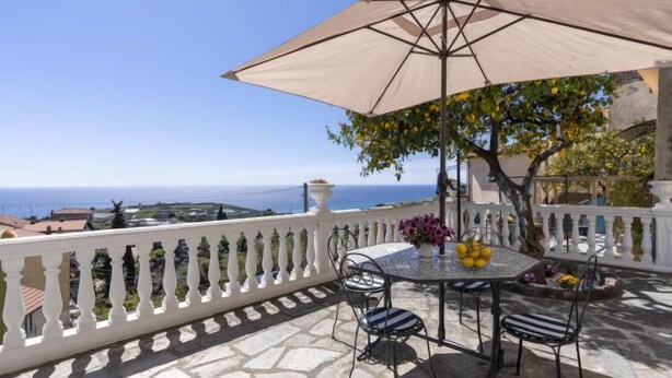 A stone-paved outdoor seating area with a table, chairs, and a large umbrella. - Il Giardino by Interhome (Terzorio)