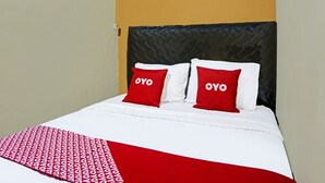 Un lit avec une tête de lit noire, une literie blanche et deux oreillers rouges sur lesquels est inscrit le mot « OYO ».