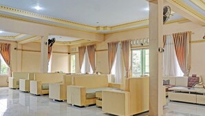 Une pièce spacieuse avec une rangée de canapés et de fauteuils de couleur beige, de grandes fenêtres avec des rideaux et un ventilateur de plafond.
