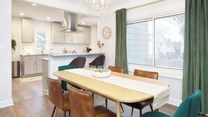 Une cuisine moderne avec des armoires blanches, une hotte en acier inoxydable et un coin repas comprenant une table et des chaises en bois.