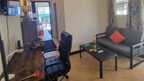Een woonkamer met een bank, een salontafel, een bureau met stoel, en een televisie.