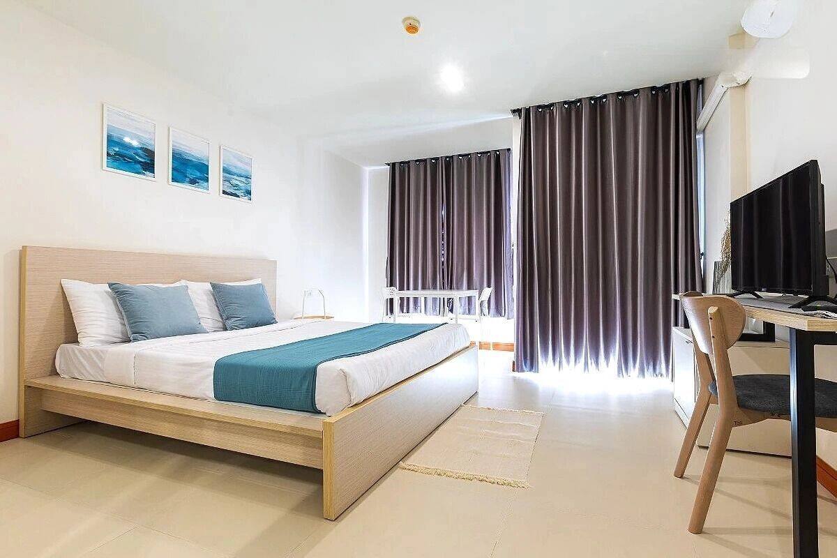 A bedroom with a bed, a desk, a chair, and a window with curtains.