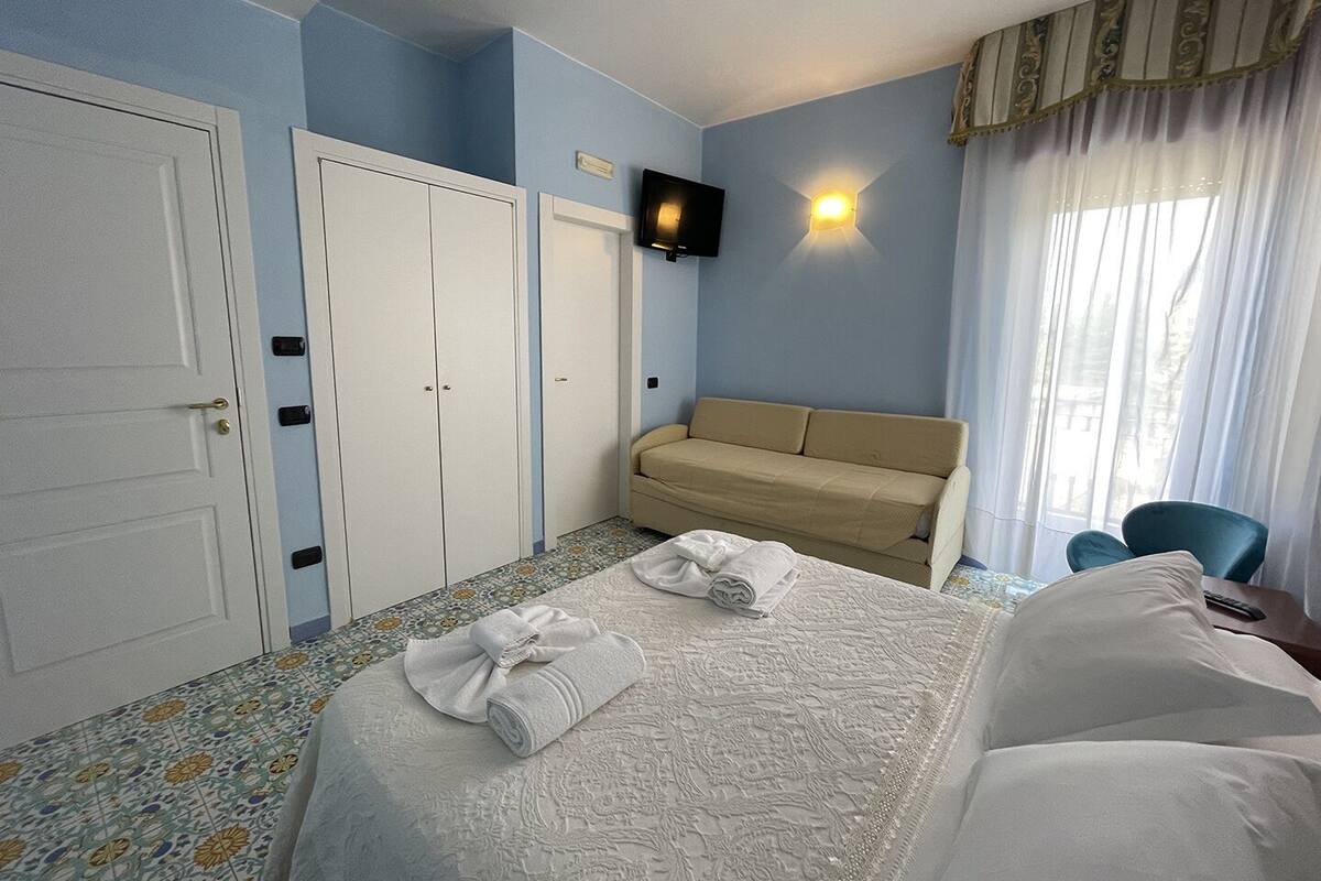 A hotel room with a bed, a sofa, a TV, and a wardrobe.