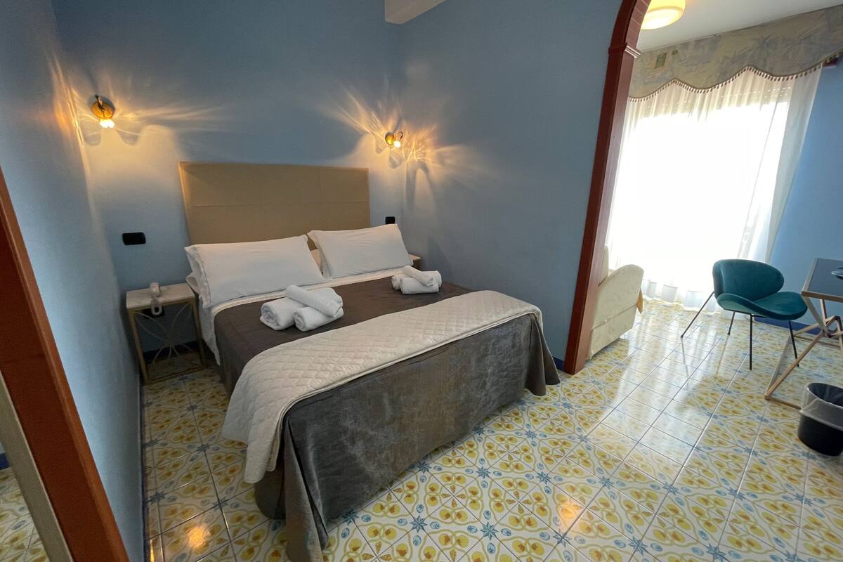 A hotel room with a bed, bedside lamps, a chair, and a window with curtains.