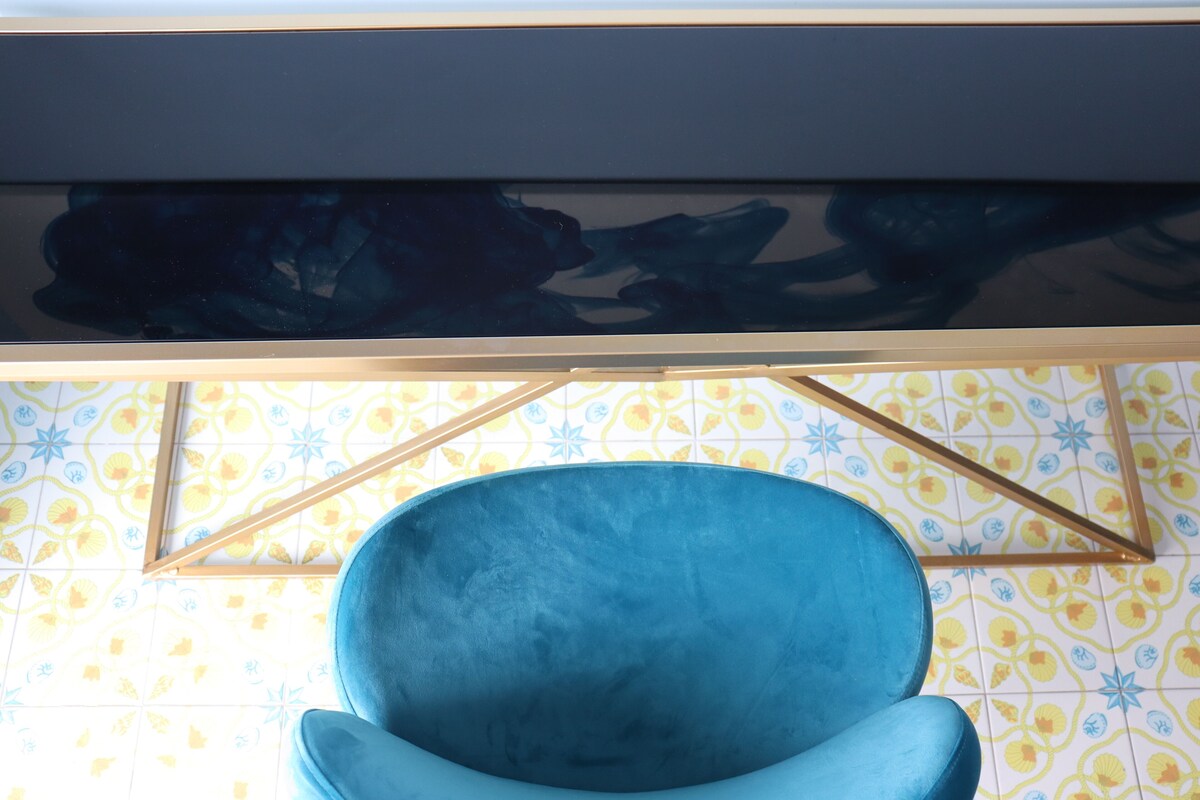 A blue chair in a room with a patterned tile floor and a dark artwork above it.