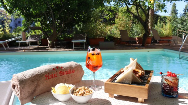 Ein Poolbereich mit Handtuch mit dem Aufdruck 'Hotel Paradise', einem Getränk, einer Speiseplatte und einer Schale Nüsse.