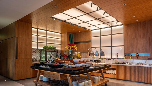 A modern kitchen with wooden accents, a central island with dishes, and a view of the adjacent dining area.