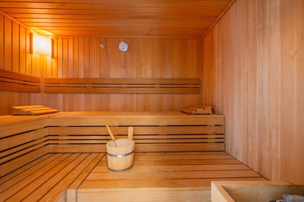 Una sauna de madera con bancos, un balde de madera y un termómetro colgado en la pared.