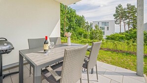 Um pátio externo com mesa, cadeiras, uma garrafa de vinho e churrasqueira.