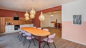Cozinha moderna com bancada de madeira, armários brancos e área de refeições com mesa de madeira e cadeiras cor-de-rosa.