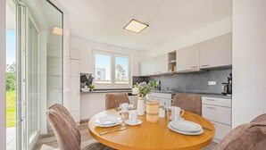 A modern kitchen with white cabinets, a round wooden dining table, and a view of the outdoors through a sliding glass door. - Hochwertiges Ferienappartement für bis zu 4 Personen in Ruhiger Wohngegend an de (Zirchow)