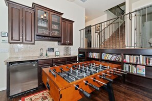 Una cocina con mesa de futbolín, armarios de madera y lavavajillas de acero inoxidable.
