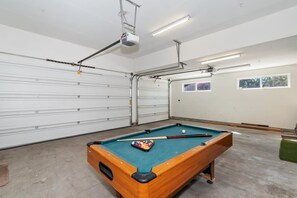 Una mesa de billar en una habitación con una puerta de garaje, iluminación en el techo y un proyector.