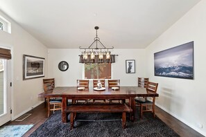 Une salle à manger avec une table en bois, des chaises, un banc, un lustre et des tableaux encadrés accrochés aux murs.
