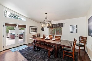 A dining area with a wooden table, chairs, a bench, a chandelier, and a view through a glass door.