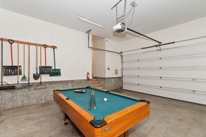 Una mesa de billar con tacos y bolas, un proyector instalado en el techo y una puerta de garaje.