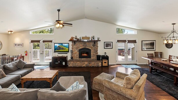 A spacious living room with a stone fireplace, comfortable seating, a television, and a ceiling fan.