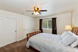 Un dormitorio con cama, ventilador de techo, ventana con cortinas y radiador.