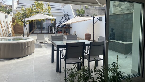 En moderne udendørs terrasse med jacuzzi, siddeområde og en Buddha-statue.