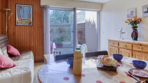 Un salon chaleureux avec un canapé, une table à manger où sont disposés des aliments pour le petit-déjeuner, un buffet en bois et une porte-fenêtre coulissante donnant sur un espace extérieur.
