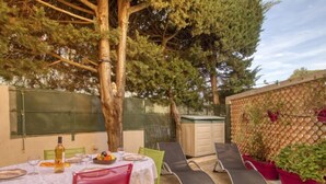 Une terrasse extérieure avec une table dressée pour le repas, entourée de chaises et d’une pergola.