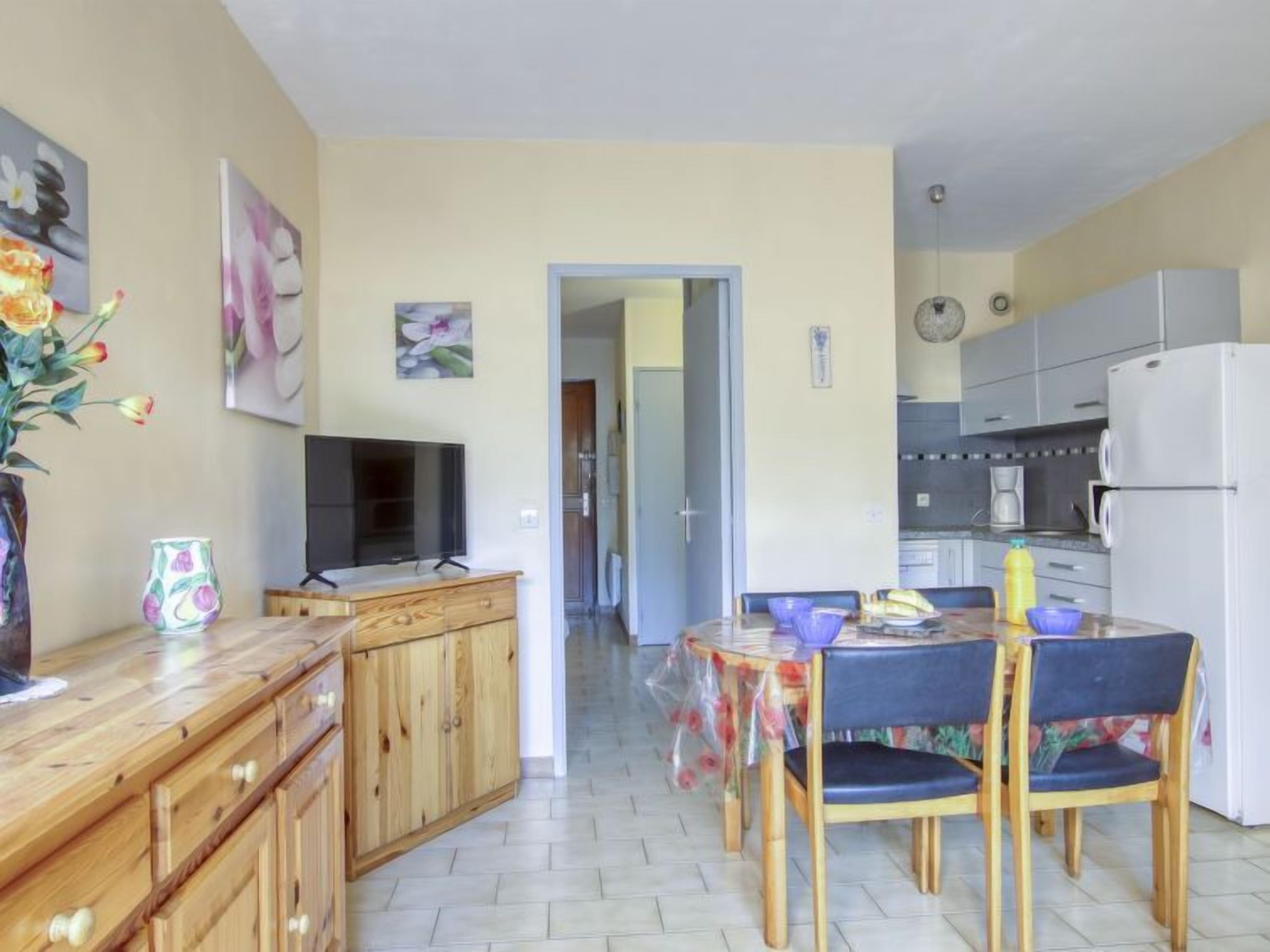 Una cucina compatta con zona pranzo, mobili in legno e una TV su un supporto.
