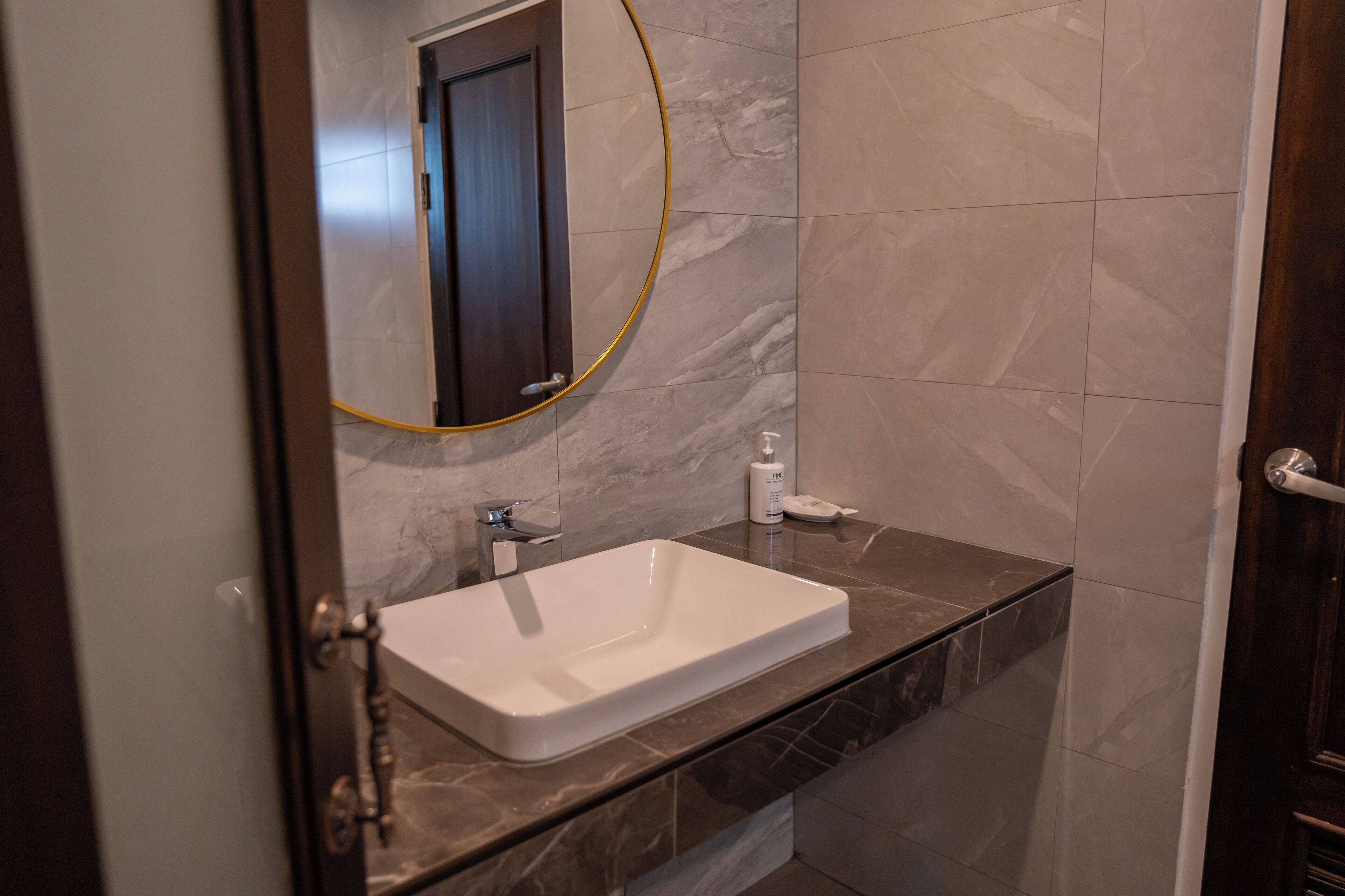 A bathroom with a white sink, a mirror, and a marble-tiled wall.