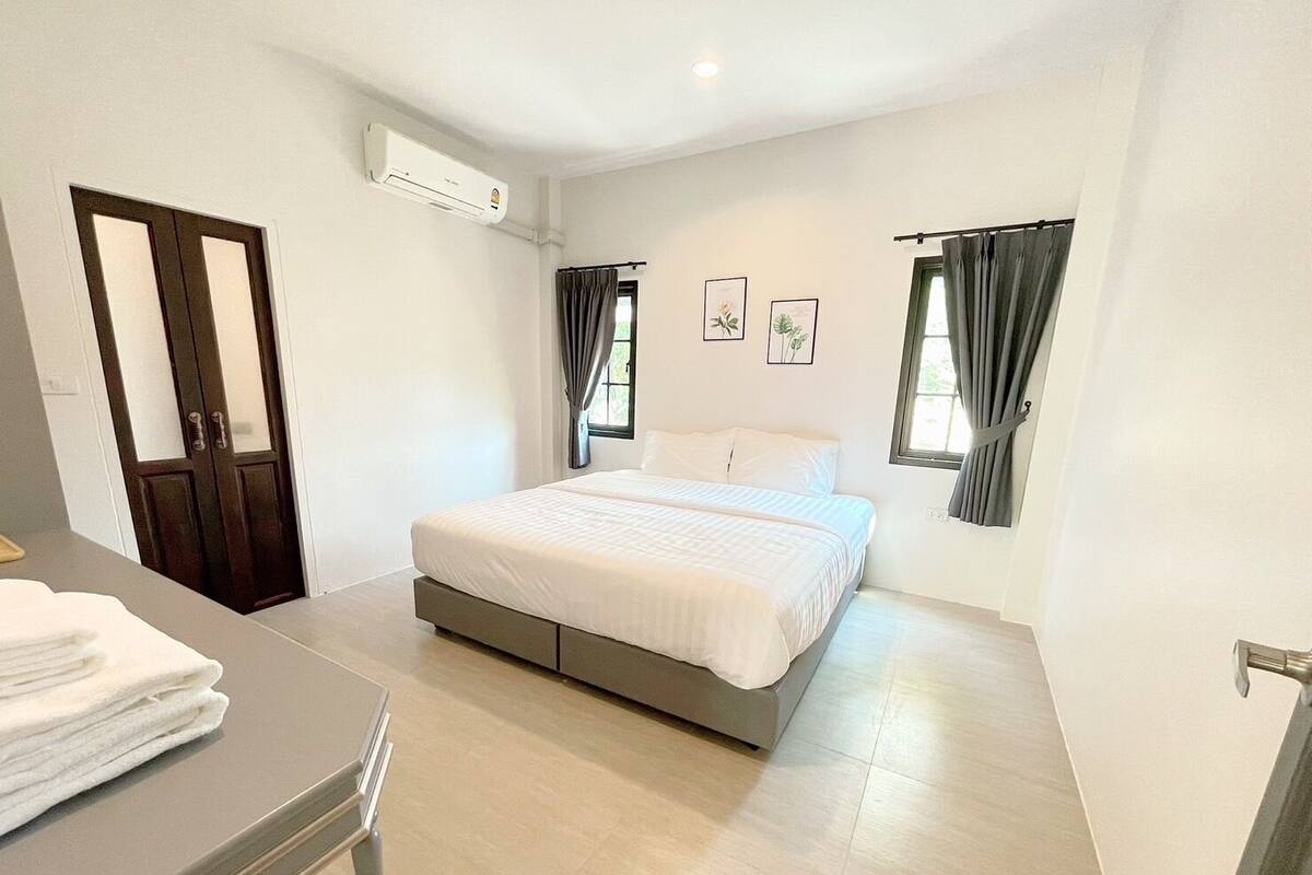 A bedroom with a bed, a desk, a chair, an air conditioning unit, and a door.