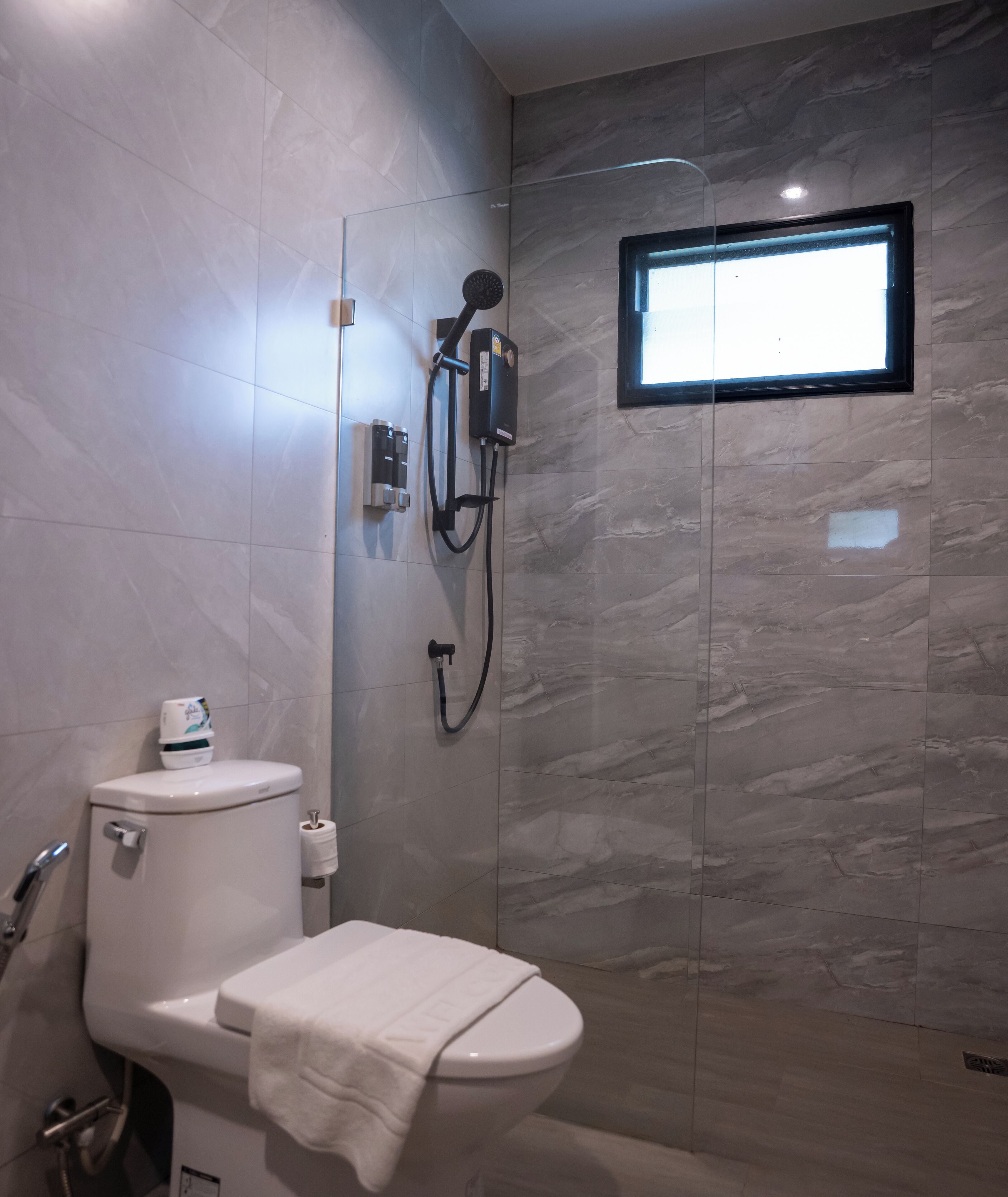A modern bathroom with a toilet, a shower with a glass enclosure, and a small window.