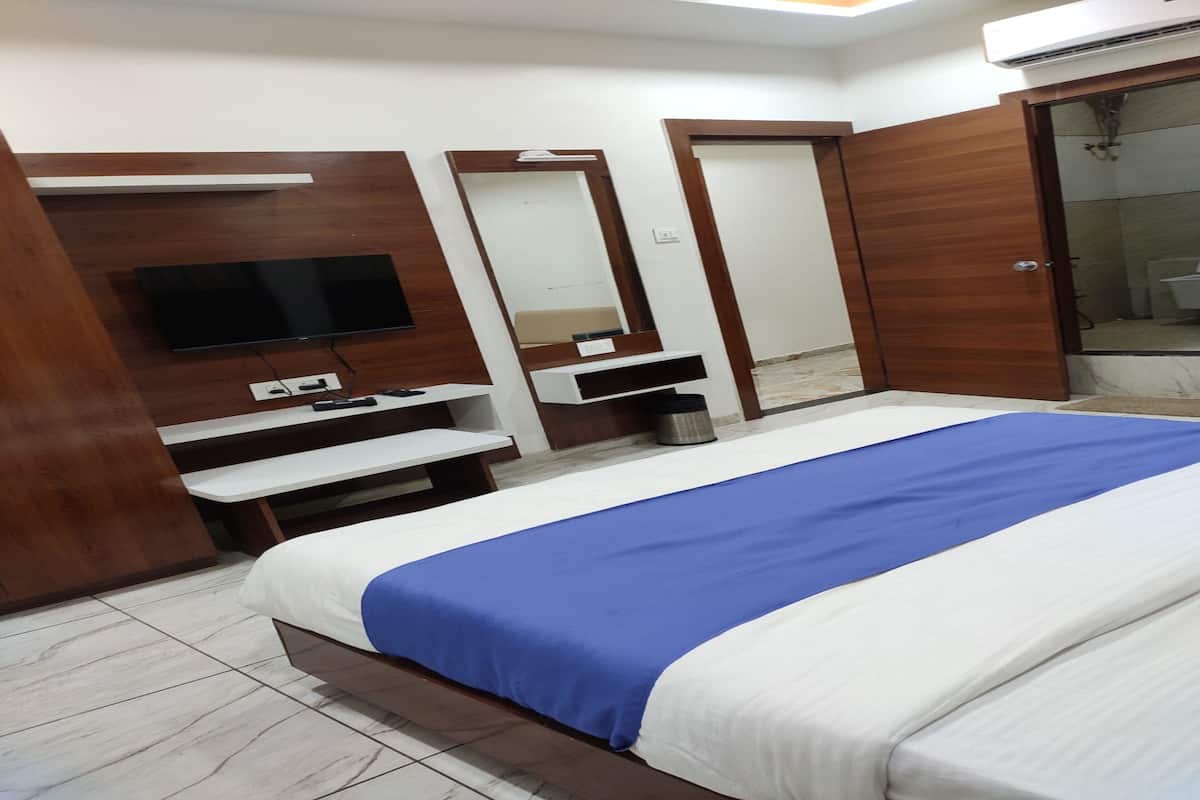 A hotel room with a bed, a TV, a mirror, a wardrobe, and a bathroom visible through an open door.