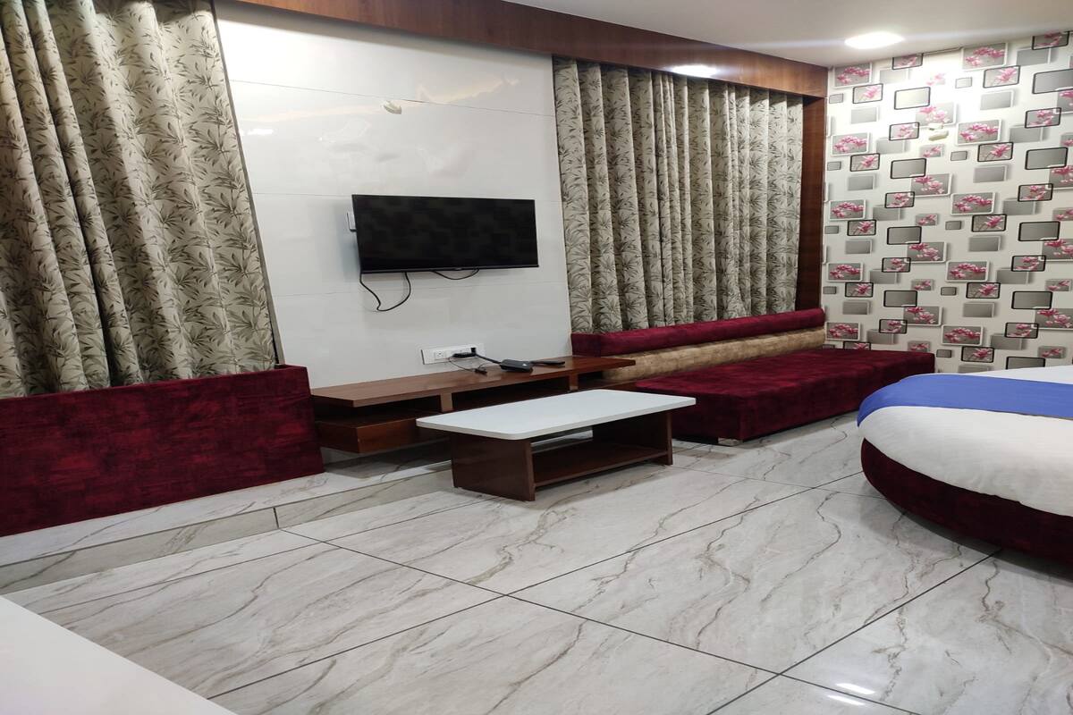 A hotel room with a flat-screen TV mounted on the wall, a wooden bench, a red sofa, and a bed with a blue and white striped bedspread.