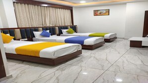 A hotel room with three beds, a small desk, and a painting on the wall. - Hotel R R One (Vadodara)