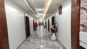 A hallway with a marble floor, wooden doors, and a white vase with flowers. - Hotel R R One (Vadodara)