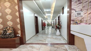 A hotel hallway with a marble floor, wooden paneling, and a reception desk with a QR code. - Hotel R R One (Vadodara)