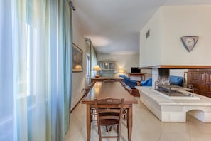Un vaste espace de vie comprenant une table à manger, des canapés bleus, une cheminée et une horloge murale.