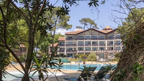 Hotel com piscina, rodeado por árvores e céu claro.