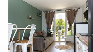 Quarto com sofá, cadeiras, uma mesinha, janela com cortinas e vista para o verde lá fora.
