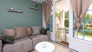 Uma sala de estar com um sofá, uma mesinha e uma janela grande com cortinas.